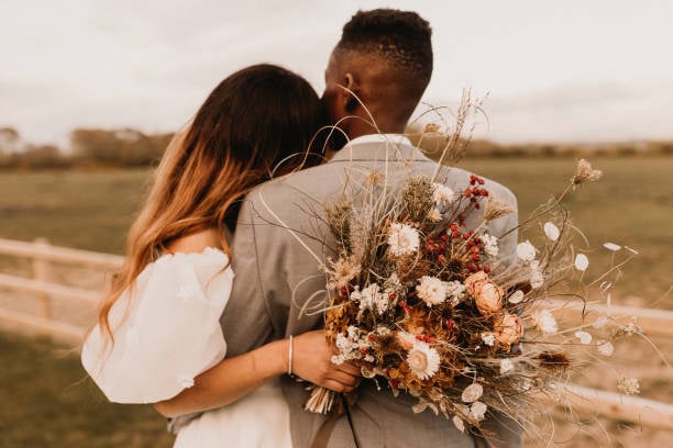 A bride and groom embracing in the field with their wedding bouquets